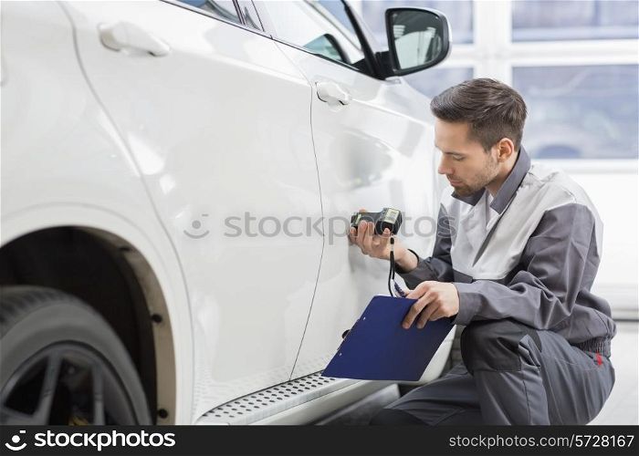 Male repair worker examining car paint with equipment in repair shop