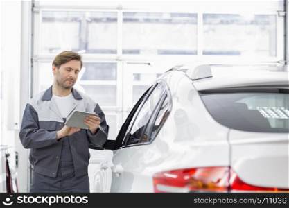 Male repair worker using tablet PC while standing by car in workshop
