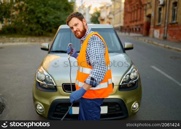 Male road worker preparing car for evacuation on tow truck fasten hook working on city street. Male road worker preparing car for evacuation