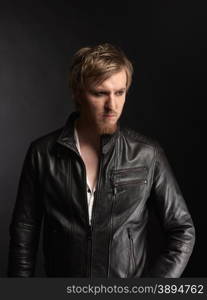 Male rocker wearing black leather jacket, dark background and studio shot