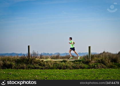 Male runner at sprinting speed training for marathon outdoors on country landscape.