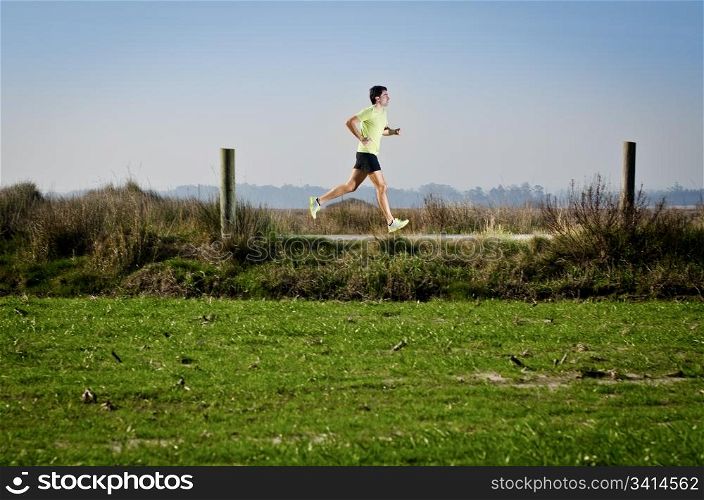 Male runner at sprinting speed training for marathon outdoors on country landscape.