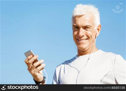 Male runner with his mobile smart phone standing outdoors. Young male runner with his mobile smart phone standing outdoors