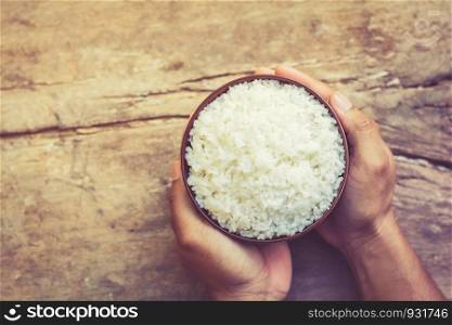 male's hand holding a bowl with cooked rice on old wooden table