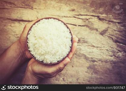 male's hand holding a bowl with cooked rice on old wooden table