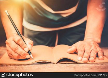 Male's hand holding pen and writing notebook on old wooden table