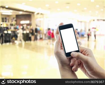 Male's hand is holding/pushing mobile phone over blurred photo of a modern shopping center, online business concept