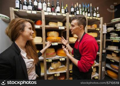 Male salesperson showing cheese to female customer in store