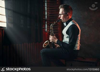 Male saxophonist playing jazz melody on saxophone against the window. Saxophonist playing jazz melody on saxophone
