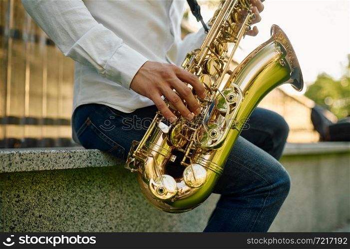 Male saxophonist plays the saxophone in summer park. Musician with sax outdoors, musical performance in nature, jazz melody performer. Male saxophonist plays the saxophone in park