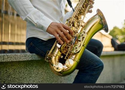 Male saxophonist plays the saxophone in summer park. Musician with sax outdoors, musical performance in nature, jazz melody performer. Male saxophonist plays the saxophone in park
