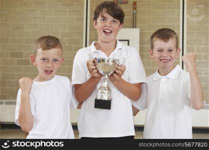Male School Sports Team In Gym With Trophy