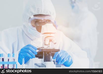 Male Scientist look into Microscope research in science laboratory. Asian scientist looking equipment laboratory chemistry labs. Covid-19 coronavirus biochemistry research experiment vaccine concept