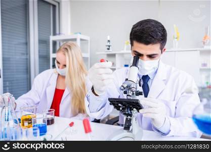Male scientist working looking at Microscope with sample test tube in a chemistry lab scientist and young female researcher are doing investigations in Laboratory analysis background