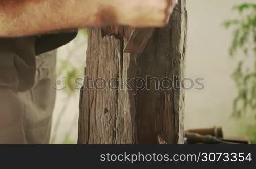 Male sculptor starting a new statue, cleaning a raw block of wood with hammer and chisel. The artist cuts some parts and leaves his tools on table.