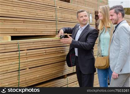 male seller and clients in wood factory yard choosing boards
