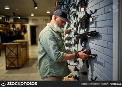 Male seller at the showcase with rifles in gun store. Weapon shop interior, ammo and ammunition assortment, firearms choice, shooting hobby and lifestyle, self protection. Male seller at showcase with rifles in gun store