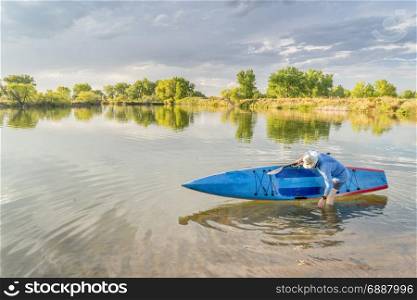 Male senior paddler rinsing his stand up paddleboard on a lake, late summer scenery in northern Colorado