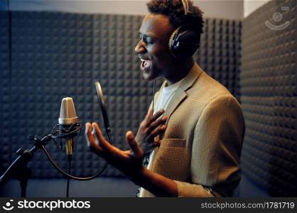 Male singer in headphones sings a song at micriphone, recording studio interior on background. Professional voice record, musician workplace, creative process, modern audio technology. Male singer sings a song, recording studio