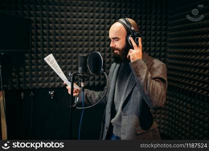 Male singer in headphones songs in audio recording studio. Musician listens composition, professional music. Male singer songs in audio recording studio