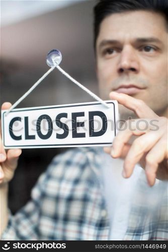 Male Small Business Owner With Serious Expression Putting Up Closed Sign During Recession Or Health Pandemic