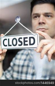 Male Small Business Owner With Serious Expression Putting Up Closed Sign During Recession Or Health Pandemic