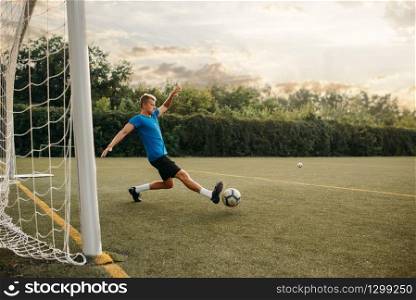 Male soccer goalkeeper hits the ball and saves the gate. Footballer on outdoor stadium, workout before game, football training