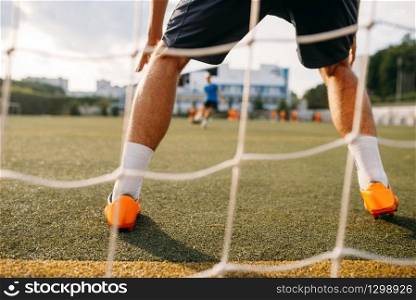 Male soccer goalkeeper stands on the gate, back view. Footballer on outdoor stadium, workout before game, football training