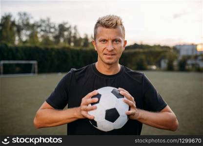 Male soccer player holding ball in hands on the field. Footballer on outdoor stadium, workout before game, football training