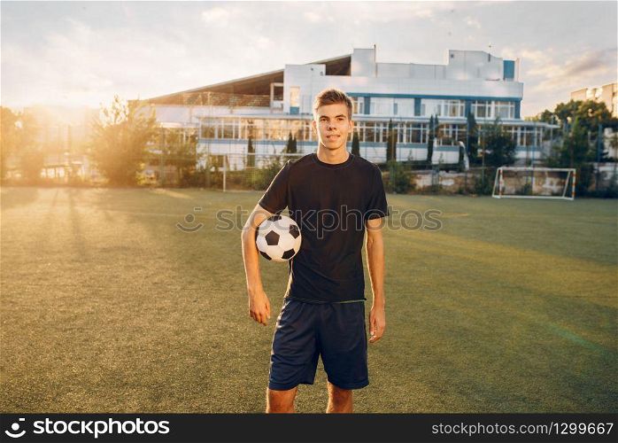 Male soccer player poses with ball in hands on the field at sunrise. Footballer on outdoor stadium, workout before game, football training