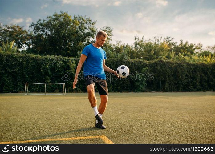 Male soccer player stuffs the ball with his foot on the field. Footballer on outdoor stadium, workout before football match