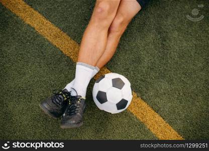 Male soccer player with ball sitting on the grass on the field. Footballer on outdoor stadium, workout before game, football training. Male soccer player with ball sitting on the grass