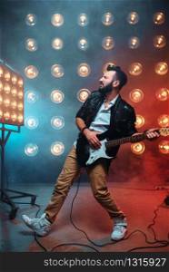 Male solo guitarist with electro guitar on the stage with the decorations of lights. Music entertainment. Bearded musican song performing