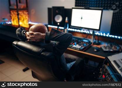 Male sound engineer at remote control panel, back view, recording studio. Musician at the mixer, professional audio processing. Male sound engineer at remote control, back view