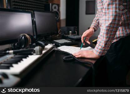 Male sound engineer hands on the table, musical keyboard, microphone and headphones on background. Digital music record studio. Media engineering