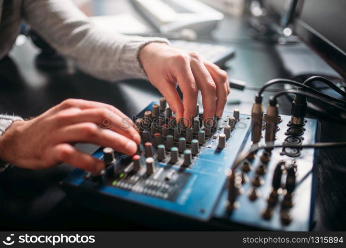 Male sound engineer hands on volume control panel. Digital music record studio. Professional audio engineering