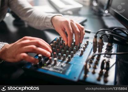 Male sound engineer hands on volume control panel. Digital music record studio. Professional audio engineering