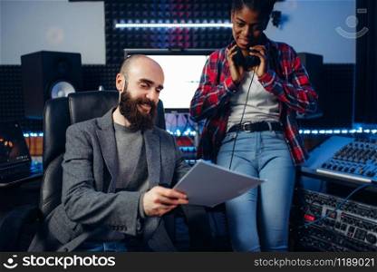 Male sound producer and female singer in headphones listens composition in recording studio. Professional audio and music mixing technology