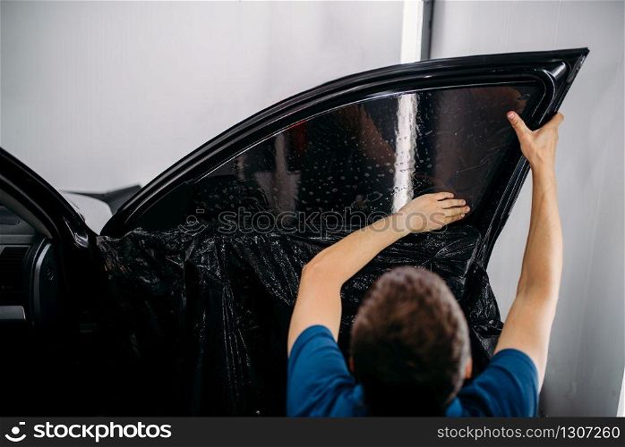 Male specialist with drier, car tinting film installation process, tinted auto glass installing procedure. Specialist with drier, tinting film installation