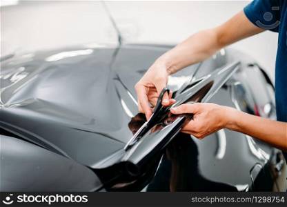 Male specialist with scissors, car tinting film installation process, tinted auto glass installing procedure
