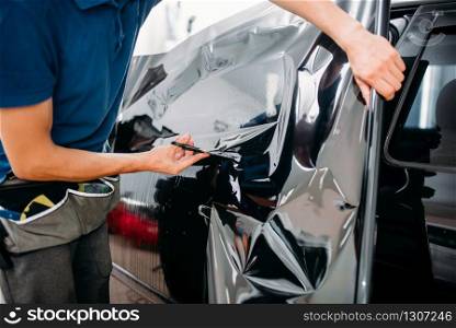 Male specialist with scissors, car tinting film installation process, tinted auto glass installing procedure. Male specialist with scissors, car tinting film