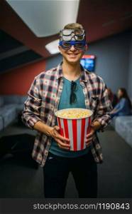 Male spectator in 3d glasses holds popcorn in cinema hall before the showtime. Man in movie theater, entertainment. Male spectator in 3d glasses, cinema hall