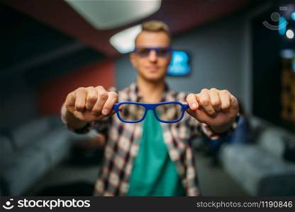 Male spectator shows 3d glasses in cinema hall before the showtime. Man in movie theater, entertainment lifestyle