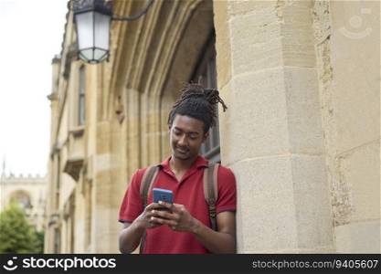 Male Student Checking Messages Or Social Media On Mobile Phone Outside University Building In Oxford UK