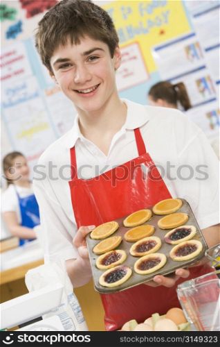 Male student holding a tray of tarts in cooking class