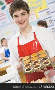 Male student holding a tray of tarts in cooking class