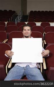 Male student holding blank board in lecture theatre, portrait