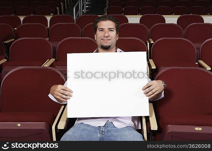 Male student holding blank board in lecture theatre, portrait