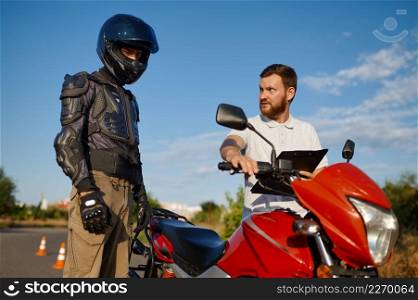 Male student in helmet and instructor, driving lesson on motordrome, motorcycle school. Training of motorcyclists beginners, biker practicing in motorschool. Driving lesson on motordrome, motorcycle school