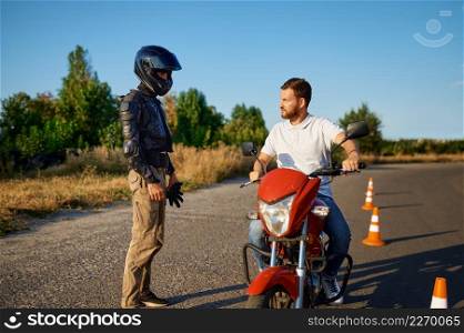 Male student in helmet and instructor, driving lesson on motordrome, motorcycle school. Training of motorcyclists beginners, biker practicing in motorschool. Male student and instructor, lesson on motordrome